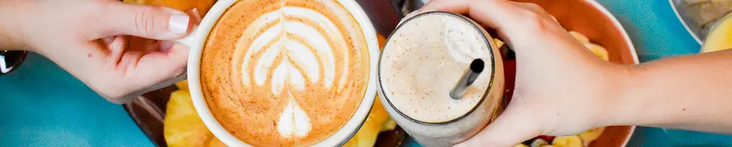 Hands clinking an iced coffee and hot latte mug Hands clinking an iced coffee and hot latte mug